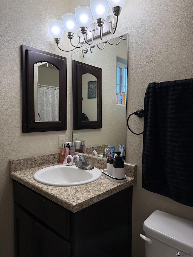 bathroom featuring a textured wall, vanity, toilet, and an inviting chandelier