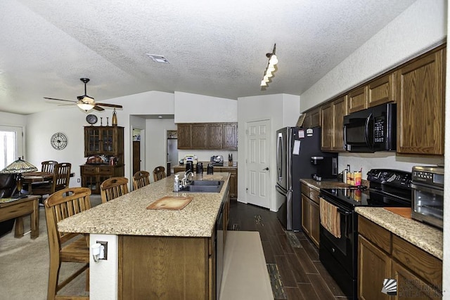 kitchen featuring a breakfast bar, a textured ceiling, sink, black appliances, and a center island with sink