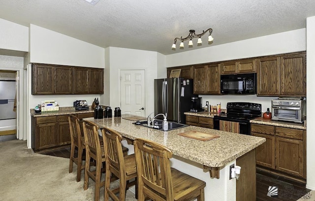 kitchen featuring a kitchen bar, a textured ceiling, sink, black appliances, and an island with sink