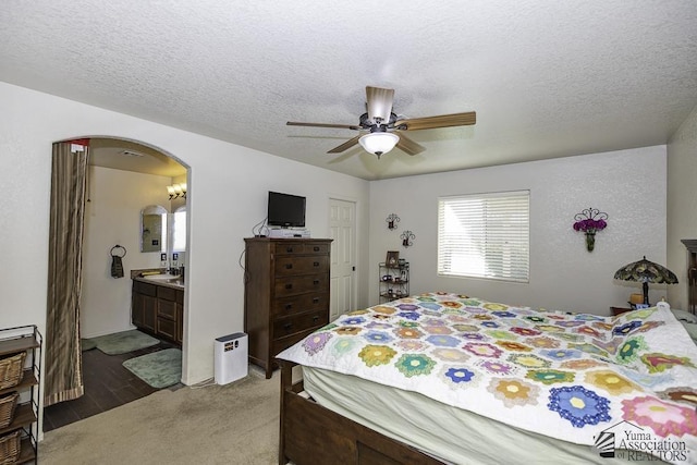 bedroom featuring ensuite bathroom, ceiling fan, a textured ceiling, and dark carpet