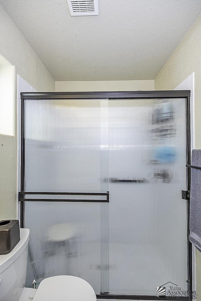 bathroom with a textured ceiling, toilet, and walk in shower