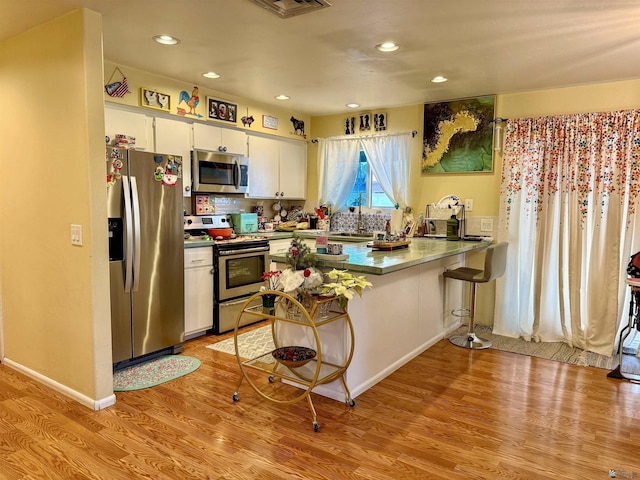 kitchen featuring sink, white cabinets, kitchen peninsula, stainless steel appliances, and light hardwood / wood-style flooring