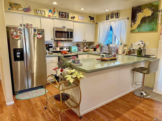 kitchen featuring stainless steel appliances, kitchen peninsula, light hardwood / wood-style flooring, and white cabinets