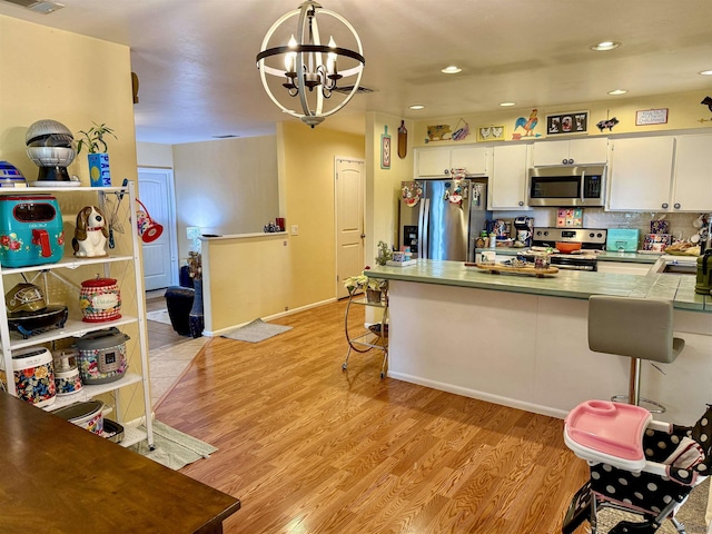 kitchen with appliances with stainless steel finishes, white cabinetry, hanging light fixtures, an inviting chandelier, and light hardwood / wood-style flooring