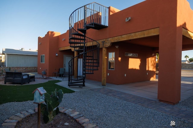 back of property featuring stucco siding, a patio, an outdoor living space, and stairs