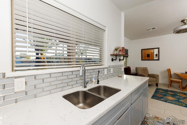 kitchen with gray cabinetry, a sink, visible vents, light stone countertops, and tasteful backsplash