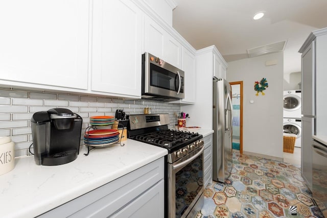 kitchen with stacked washer and clothes dryer, stainless steel appliances, visible vents, decorative backsplash, and light stone countertops