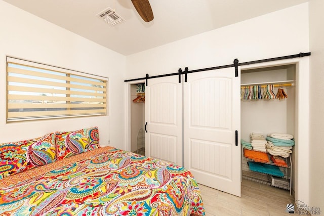 bedroom with a barn door, visible vents, a ceiling fan, light wood-style flooring, and a closet