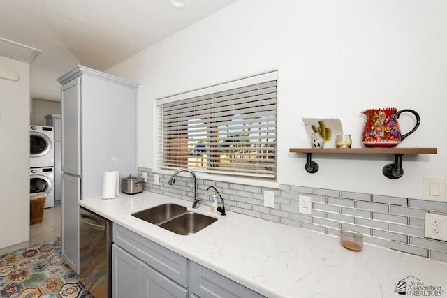 kitchen with stacked washer / dryer, a sink, stainless steel dishwasher, light stone countertops, and tasteful backsplash