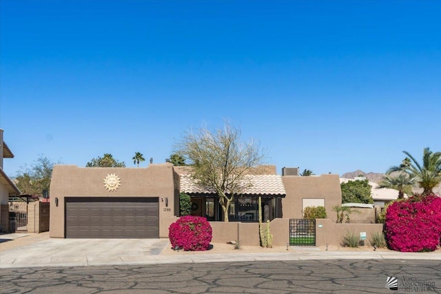 southwest-style home featuring concrete driveway, an attached garage, a gate, and stucco siding