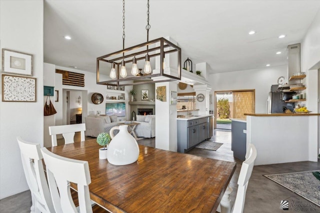 dining room featuring a lit fireplace, concrete flooring, and recessed lighting