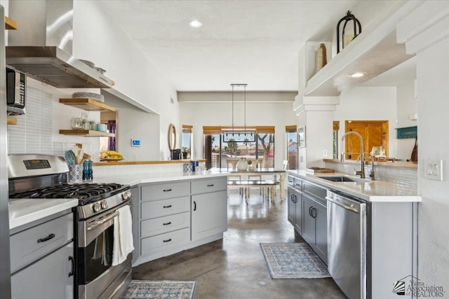 kitchen with appliances with stainless steel finishes, a peninsula, gray cabinets, wall chimney range hood, and a sink