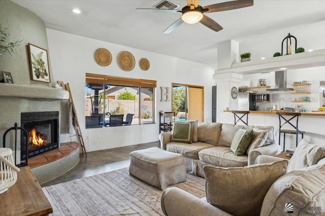 living room with ceiling fan, concrete flooring, recessed lighting, visible vents, and a lit fireplace