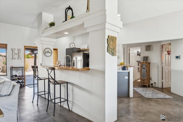 kitchen featuring a breakfast bar, stainless steel fridge, finished concrete flooring, and a high ceiling