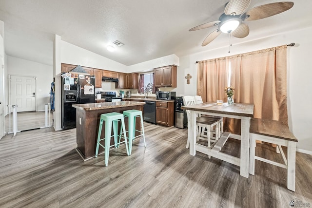 kitchen featuring lofted ceiling, under cabinet range hood, a breakfast bar, a center island, and black appliances