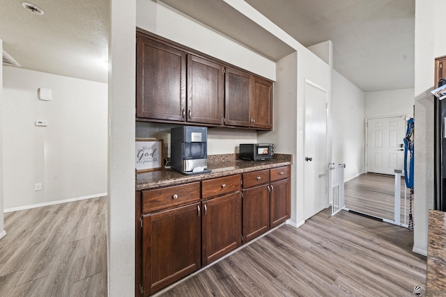 kitchen with dark stone countertops, light wood-style flooring, and dark brown cabinets