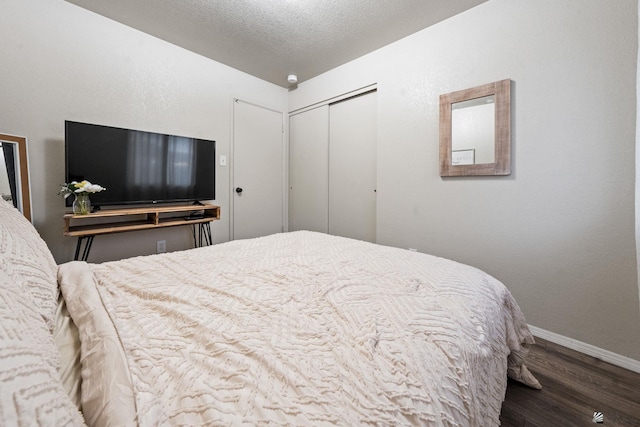 bedroom with a closet, dark wood finished floors, a textured ceiling, and baseboards