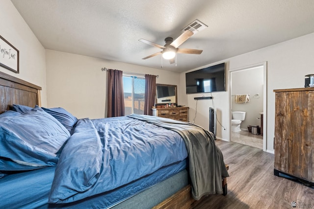 bedroom featuring visible vents, a ceiling fan, ensuite bath, wood finished floors, and a textured ceiling