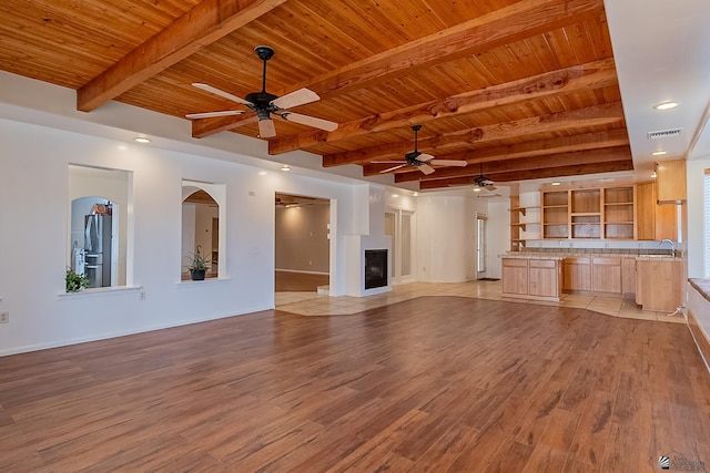 unfurnished living room with beam ceiling, wood ceiling, light hardwood / wood-style flooring, and ceiling fan