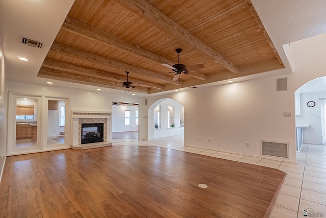 unfurnished living room with a tile fireplace, beamed ceiling, ceiling fan, wood ceiling, and light wood-type flooring