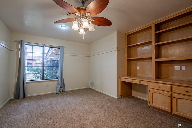 interior space featuring ceiling fan, built in desk, and light carpet