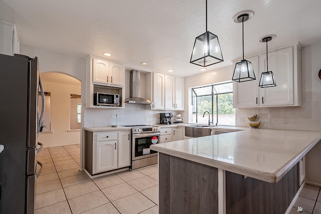 kitchen with white cabinets, hanging light fixtures, kitchen peninsula, stainless steel appliances, and wall chimney exhaust hood