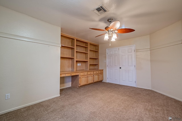 interior space featuring light carpet, built in desk, and ceiling fan