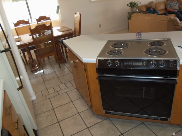 kitchen with brown cabinetry, light countertops, electric range, and light tile patterned floors