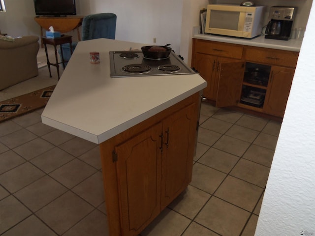 kitchen featuring light tile patterned floors, light countertops, white microwave, brown cabinetry, and stovetop