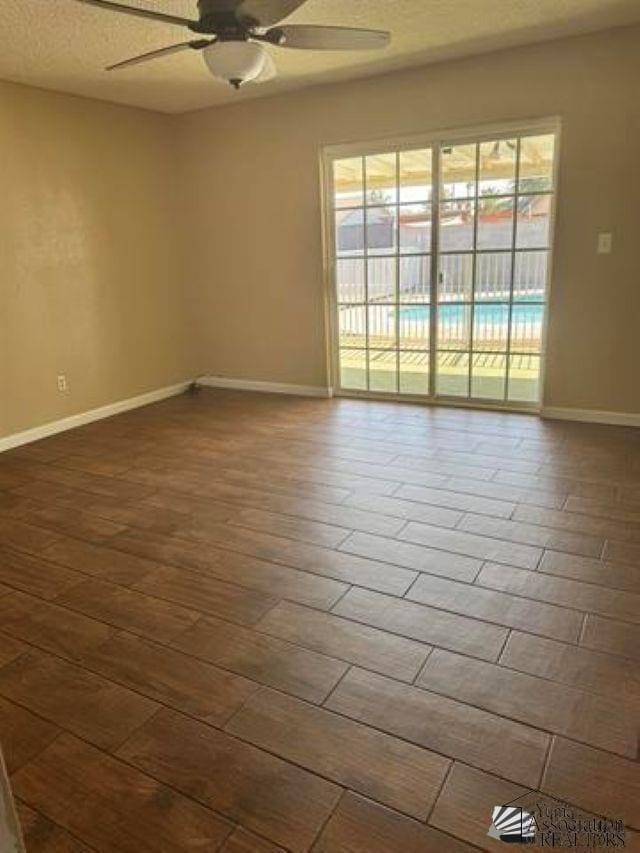 empty room featuring dark wood-style floors, ceiling fan, a textured ceiling, and baseboards