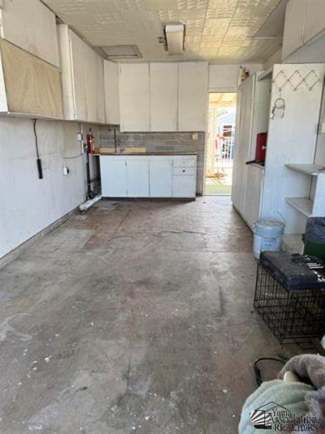 kitchen featuring unfinished concrete floors and white cabinetry