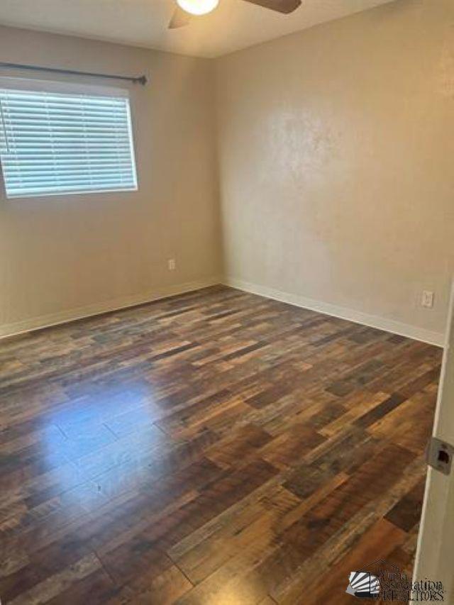 spare room with ceiling fan, baseboards, and dark wood-style flooring