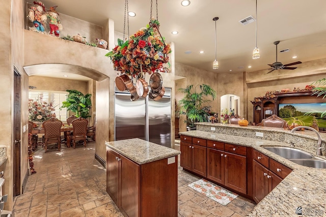 kitchen featuring hanging light fixtures, a center island, ceiling fan, light stone counters, and sink