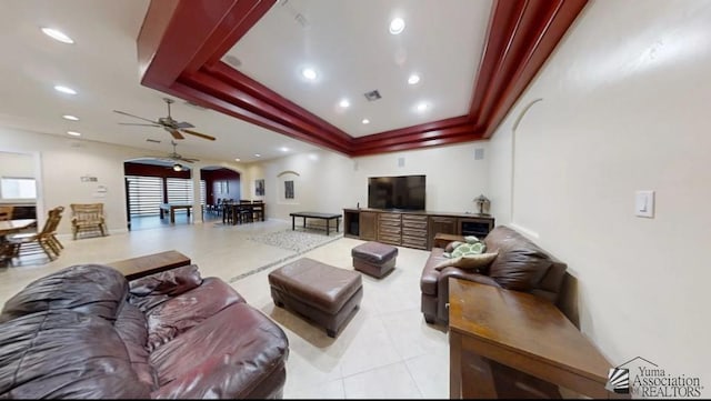 living room with a raised ceiling, ceiling fan, and light tile patterned floors