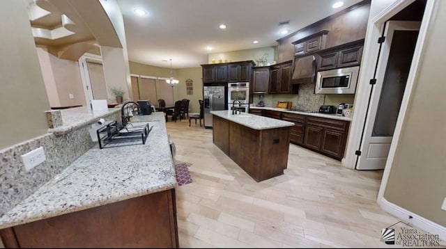 kitchen with decorative backsplash, appliances with stainless steel finishes, dark brown cabinets, a kitchen island with sink, and pendant lighting