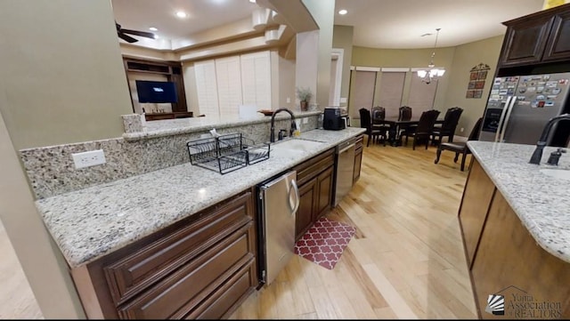 kitchen featuring light stone countertops, appliances with stainless steel finishes, ceiling fan with notable chandelier, sink, and light hardwood / wood-style flooring