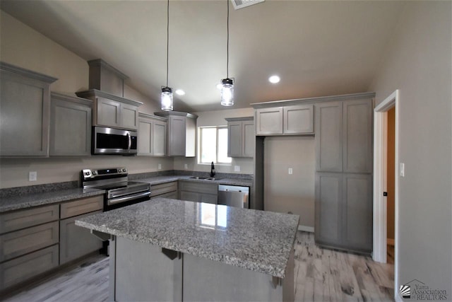 kitchen featuring a center island, gray cabinets, appliances with stainless steel finishes, a sink, and vaulted ceiling