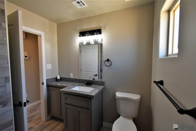 bathroom featuring baseboards, visible vents, toilet, wood finished floors, and vanity