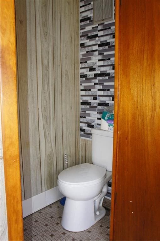 bathroom with tile patterned floors, wood walls, and toilet