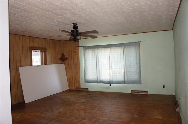 unfurnished room with wood walls, ceiling fan, and dark hardwood / wood-style floors