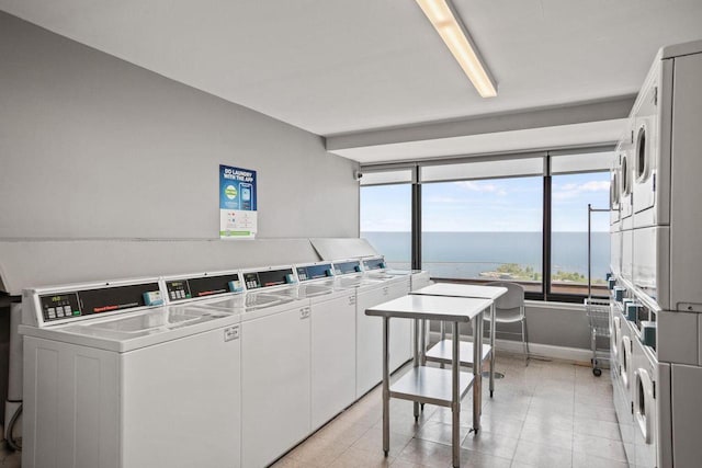 community laundry room featuring a water view, baseboards, washer and dryer, and stacked washer / dryer