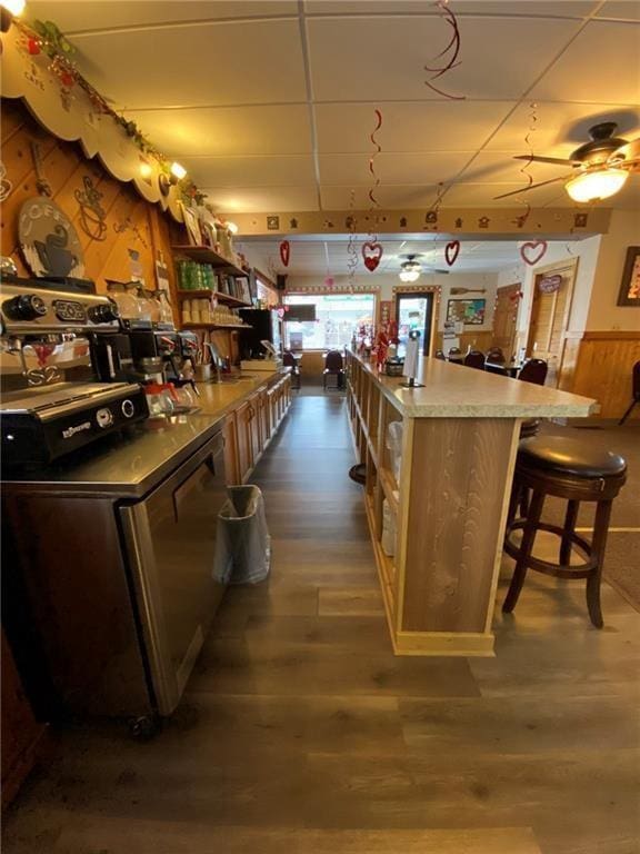 kitchen with a drop ceiling, a breakfast bar area, a center island, wood-type flooring, and ceiling fan