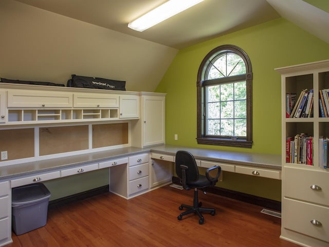 unfurnished office featuring a healthy amount of sunlight, vaulted ceiling, built in desk, and hardwood / wood-style floors