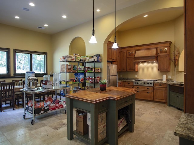 kitchen with stainless steel appliances, premium range hood, dark stone countertops, light tile floors, and decorative light fixtures