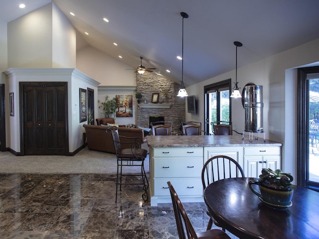 kitchen featuring high vaulted ceiling, ceiling fan, a stone fireplace, white cabinets, and light stone counters