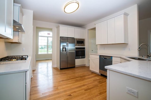 kitchen with sink, light wood-type flooring, stainless steel appliances, white cabinets, and wall chimney exhaust hood