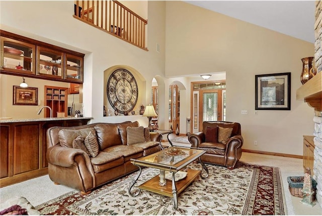 living room featuring high vaulted ceiling, light colored carpet, a stone fireplace, and sink