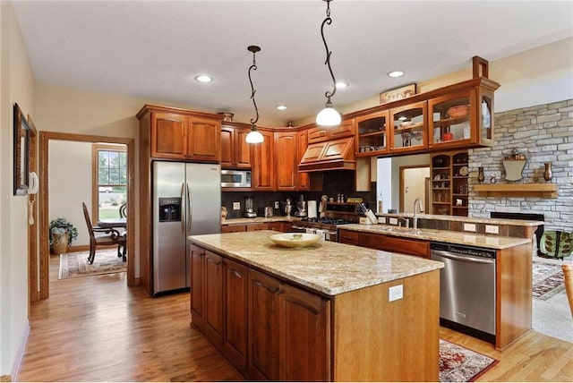 kitchen with appliances with stainless steel finishes, a kitchen island, hanging light fixtures, and light hardwood / wood-style flooring