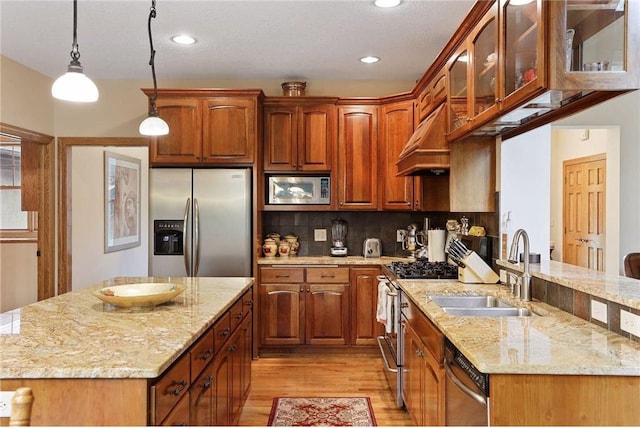 kitchen with hanging light fixtures, a center island, stainless steel appliances, sink, and light hardwood / wood-style flooring