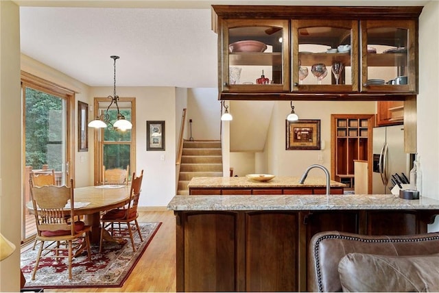 kitchen featuring hanging light fixtures, light wood-type flooring, a notable chandelier, stainless steel fridge with ice dispenser, and light stone countertops